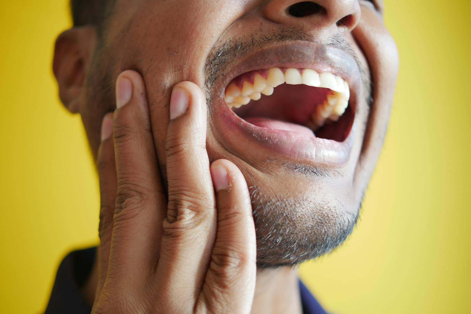 Gros plan d'un homme se tenant la joue, affichant une bouche grande ouverte sur un fond jaune.