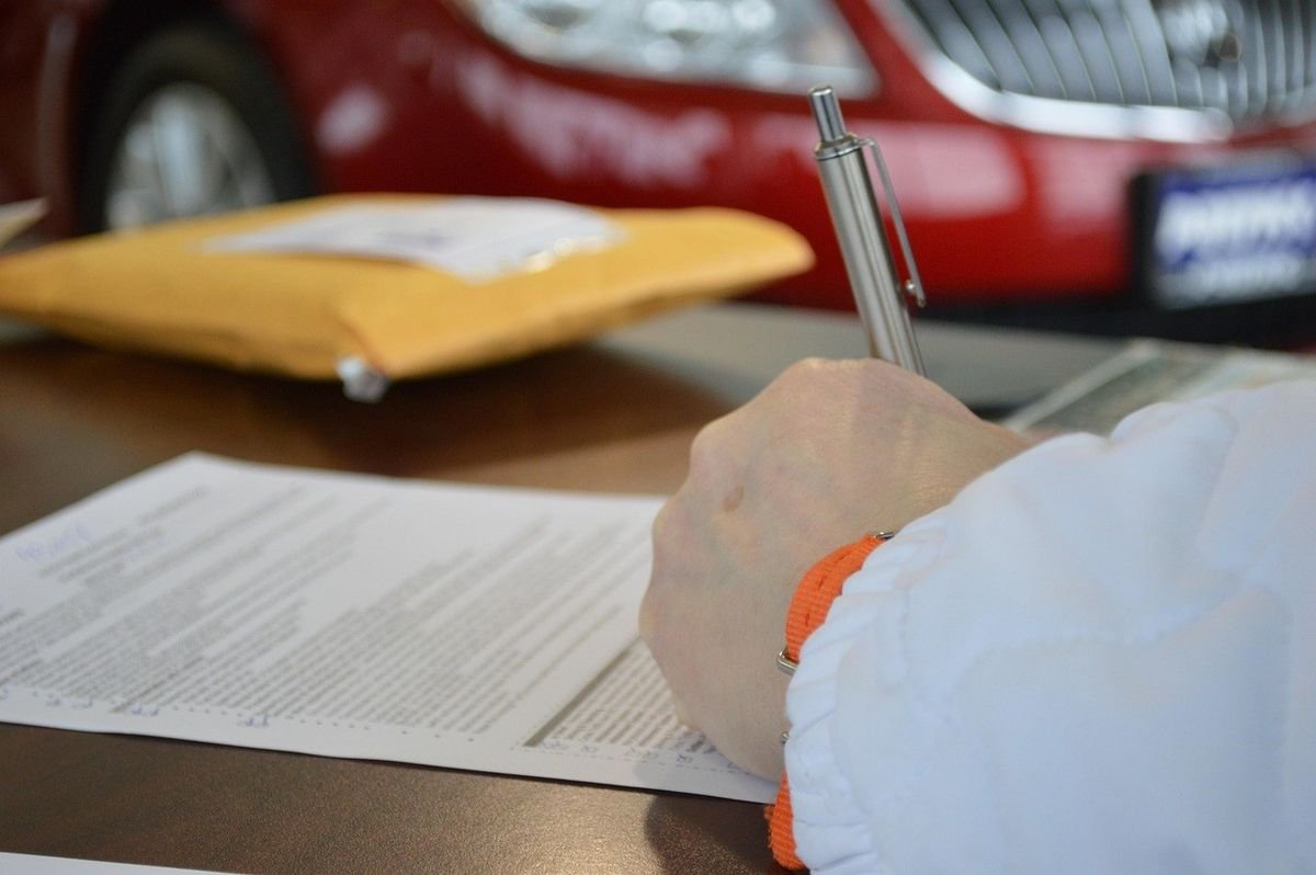 Main tenant un stylo sur un document, enveloppe jaune et voiture rouge en arrière-plan Main tenant un stylo sur un document, enveloppe jaune et voiture rouge en arrière-plan