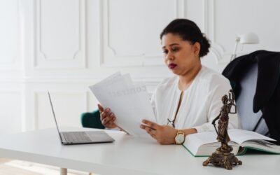 Femme en blouse blanche lit des documents à un bureau avec ordinateur et statue en bronze