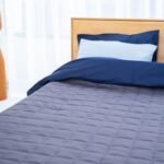 Un lit avec draps bleus, oreillers, lampe en bois et fenêtre