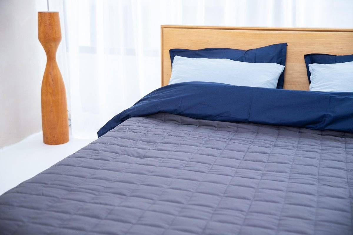 Un lit avec draps bleus, oreillers, lampe en bois et fenêtre