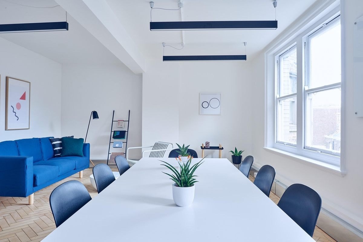 Salle de réunion avec table blanche, chaises bleues, canapé bleu, plantes, fenêtres, éclairage suspendu
