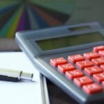 Calculatrice avec boutons rouges, stylo et feuille sur une table