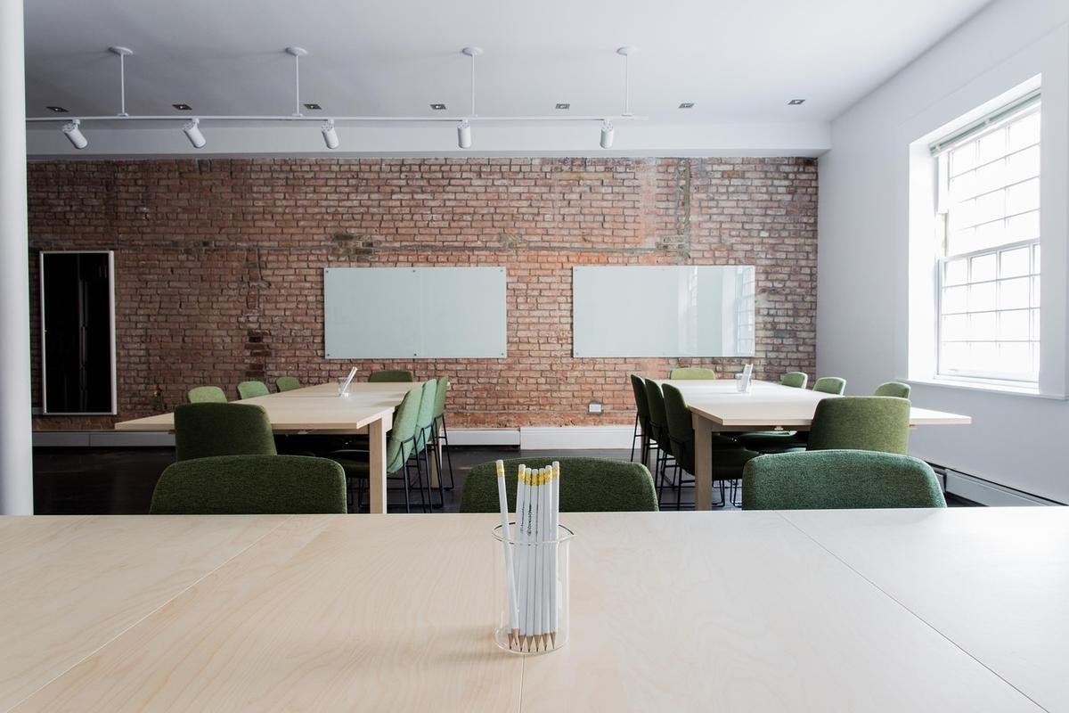 Salle de réunion avec tables blanches, chaises vertes, mur de briques rouges et tableaux blancs