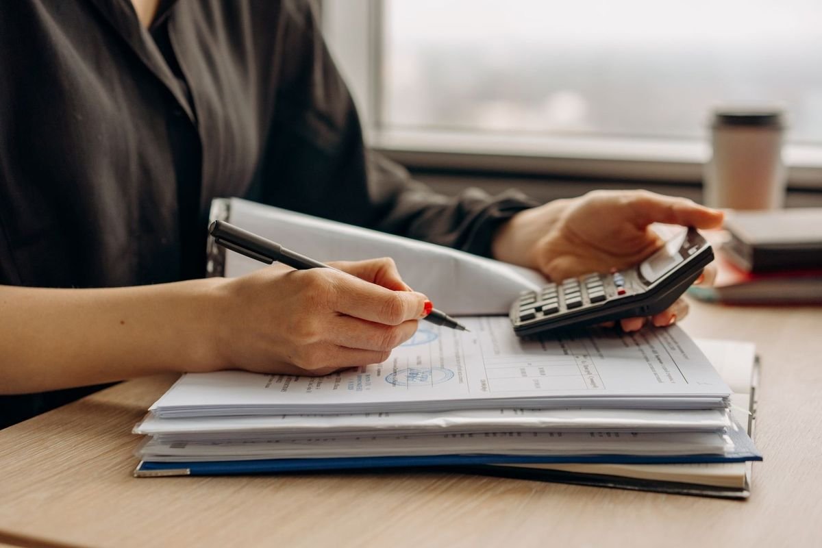 Individu prenant des notes avec une calculatrice sur une table près d'une fenêtre