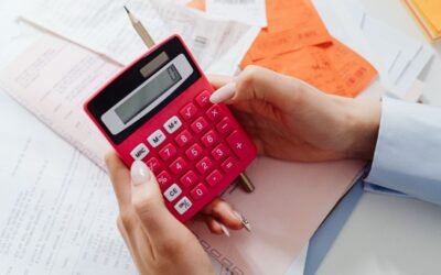 Des mains manipulent une calculatrice rouge au-dessus de documents et d'un crayon sur une table