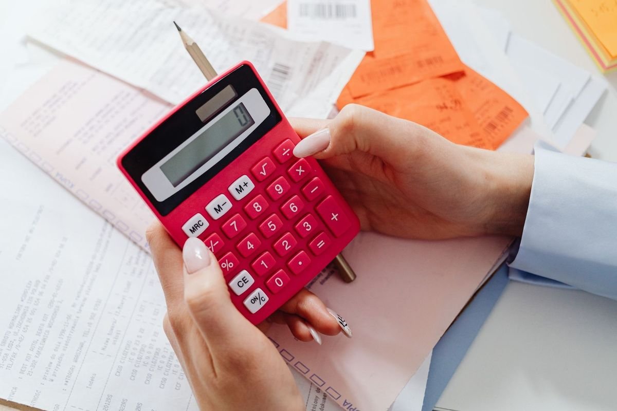 Des mains manipulent une calculatrice rouge au-dessus de documents et d'un crayon sur une table