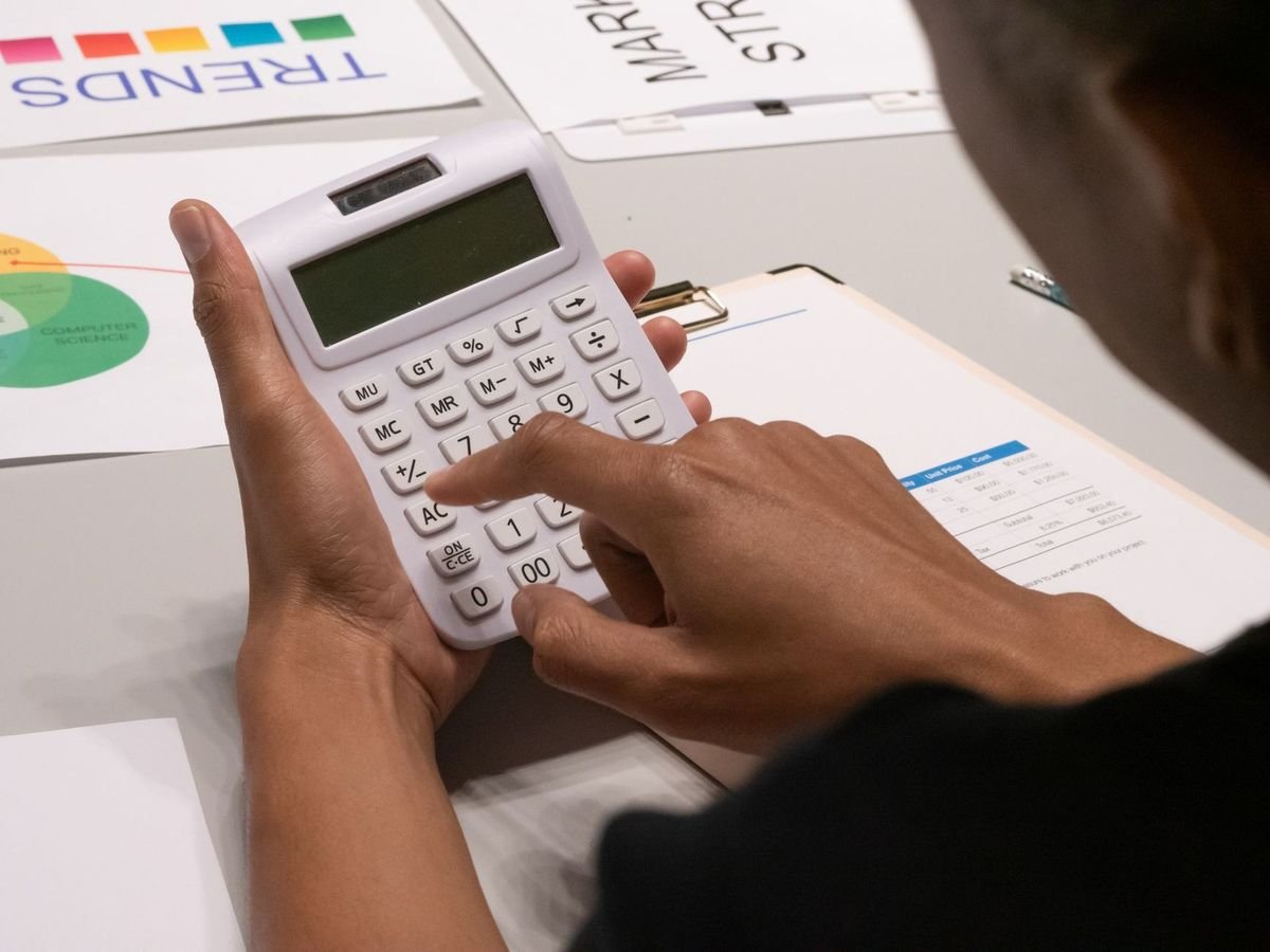 Une personne manipule une calculatrice sur une table avec des documents et graphiques colorés